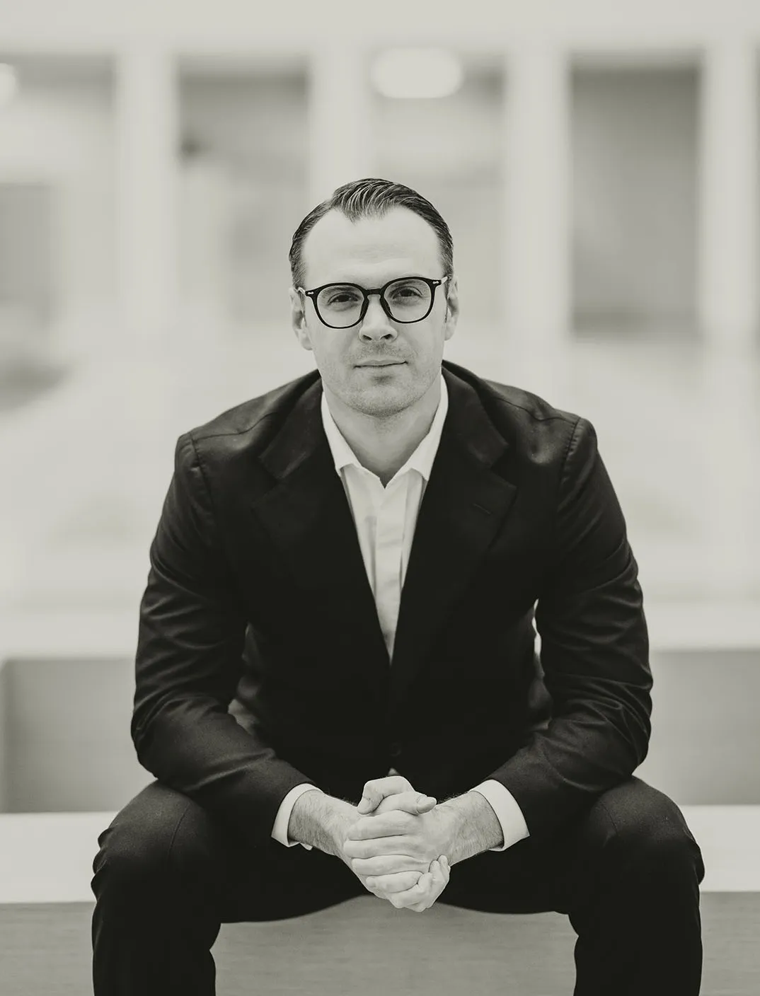 Fotografie von Rechtsanwalt Franz Stöger. Er sitzt mit verschränkten Händen auf einer niedrigen Mauer und schaut direkt in die Kamera.